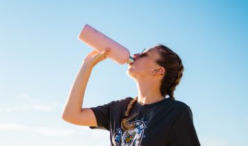 woman drinking water using pink bottle beside sea during daytime
