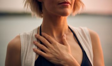 woman in white vest and black bikini with hand on chest